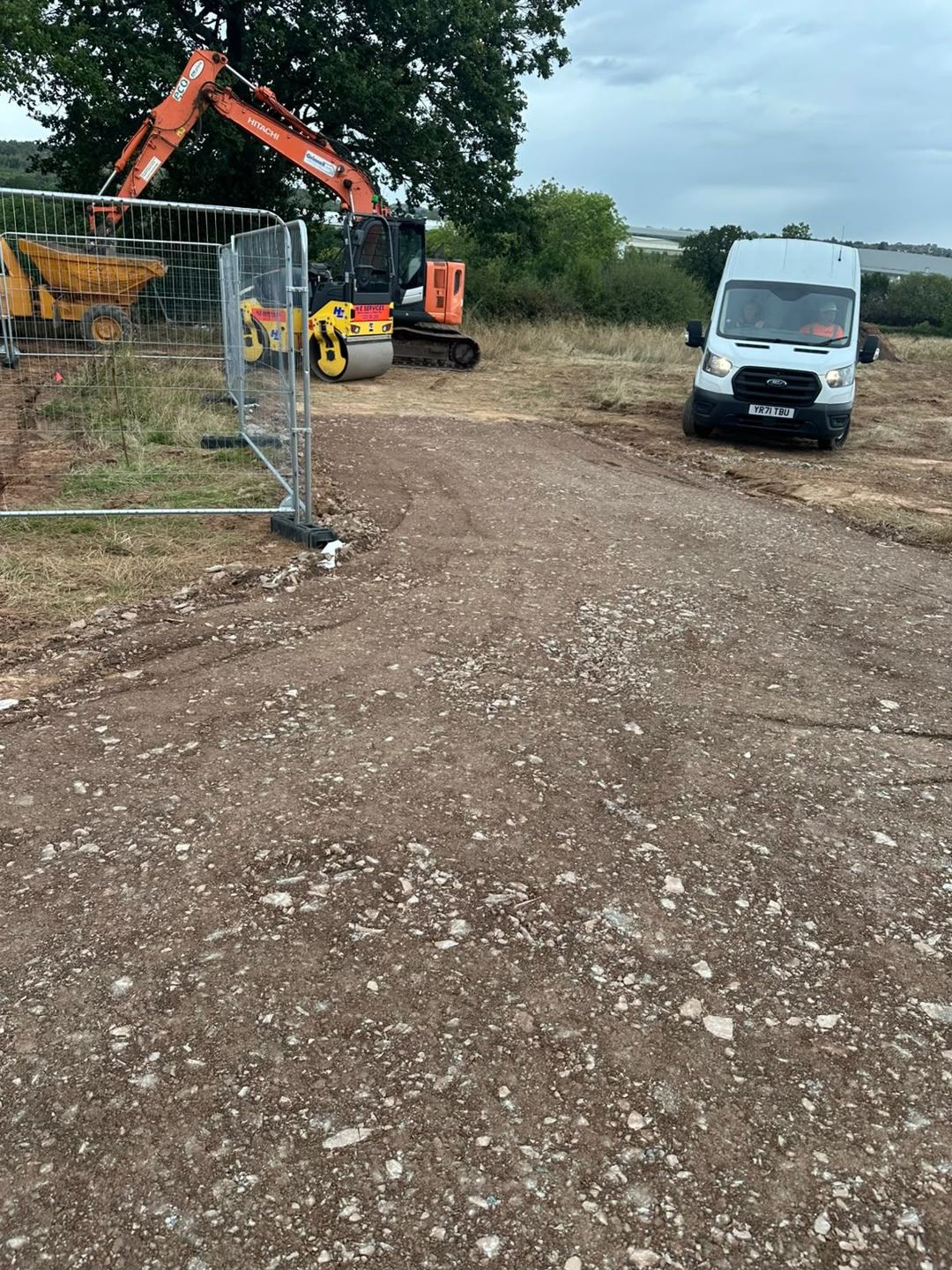 A newly built stone access track leading to a fenced site compound with an excavator and dumper.