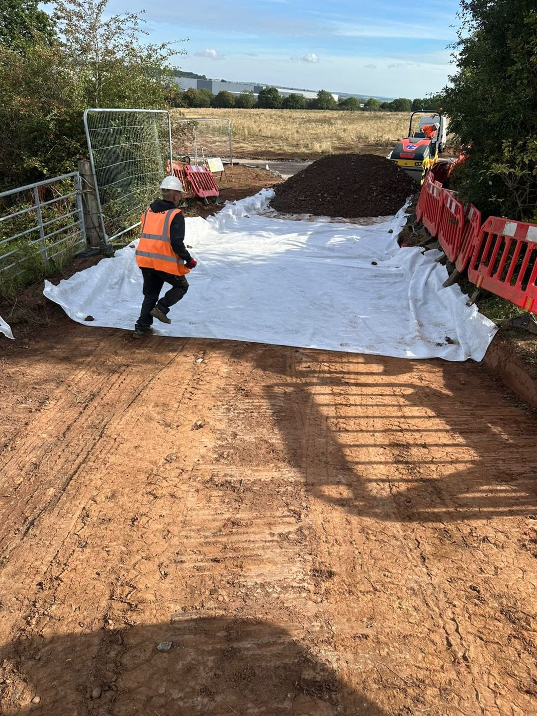 An operative laying geotextile membrane across the stripped formation of a new access track.