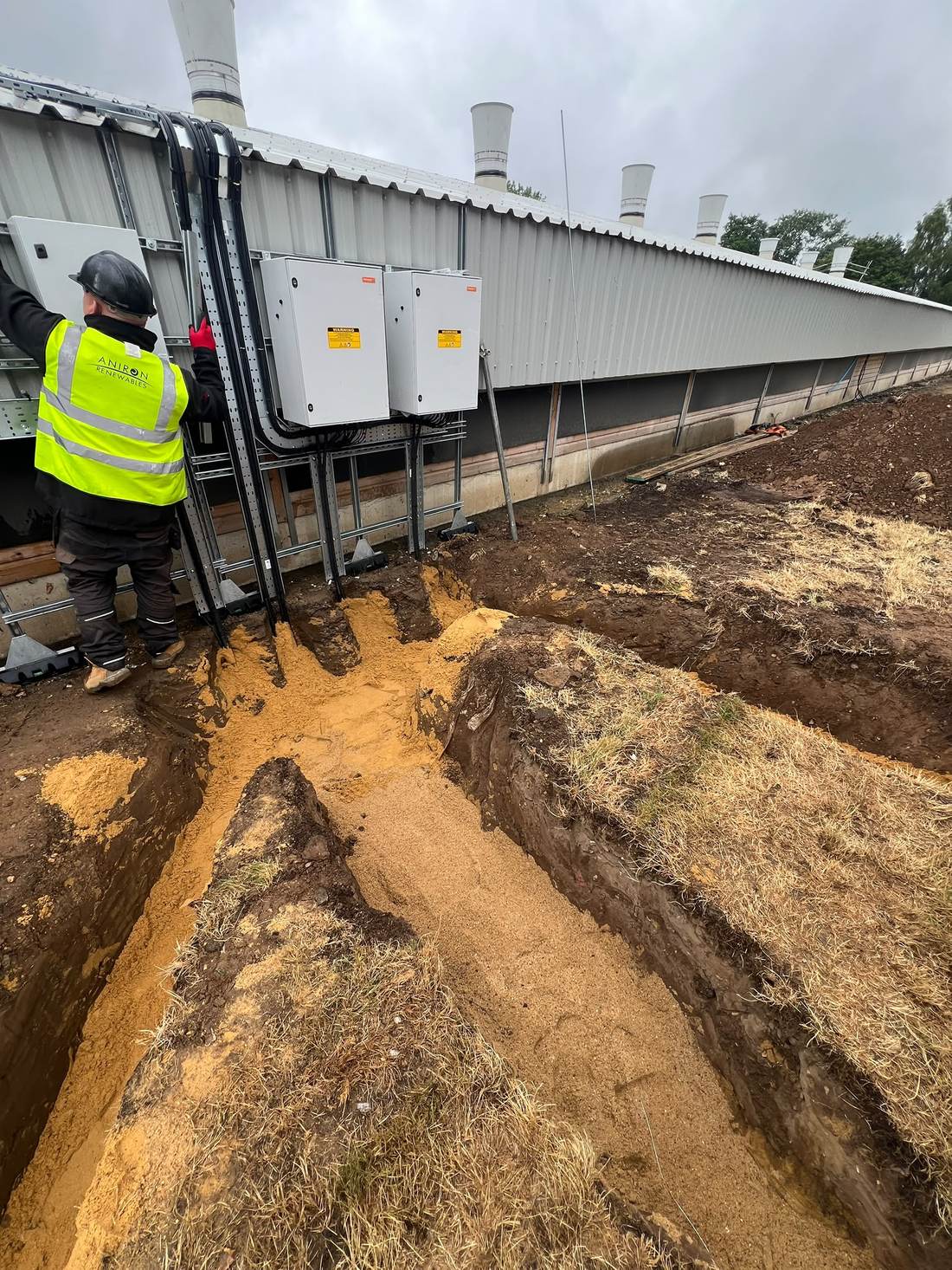 An installation team member working on switchgear enclosures above a cable trench at Amber Farm, Norfolk.