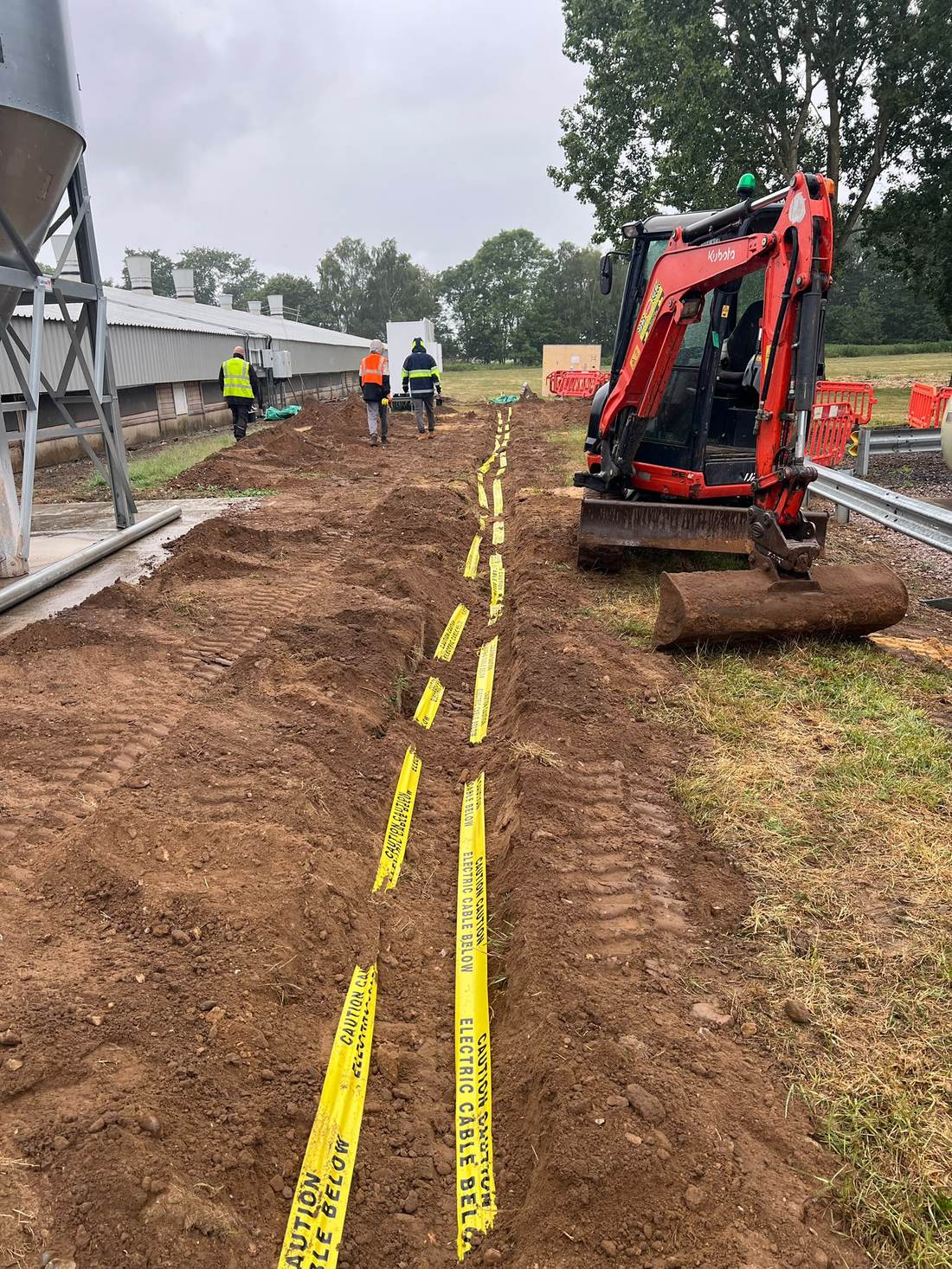 A mini excavator alongside a trench marked with electric cable warning tape at Amber Farm, Norfolk.
