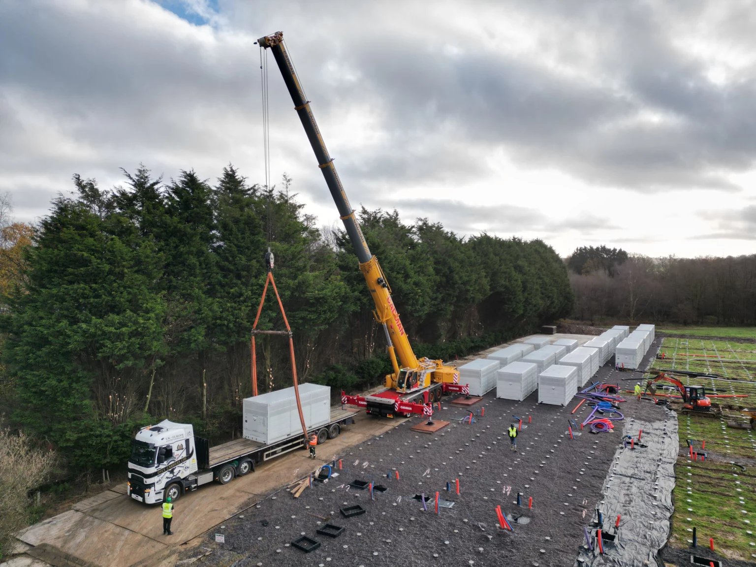 A mobile crane lifting a battery storage container into place on screw pile foundations at a BESS site.
