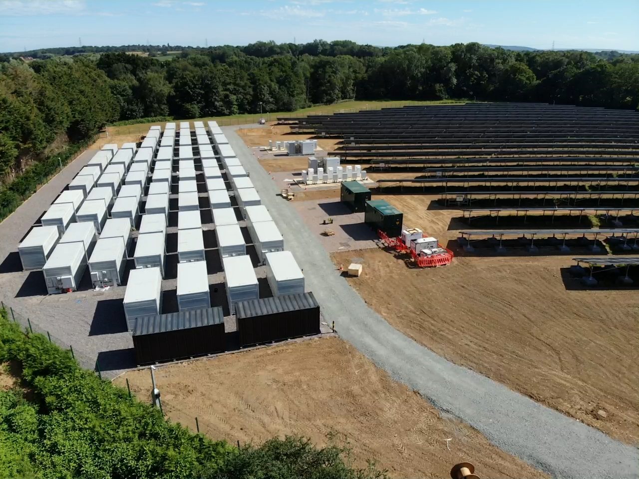 Aerial view of rows of battery energy storage containers alongside a solar array on a completed BESS site.