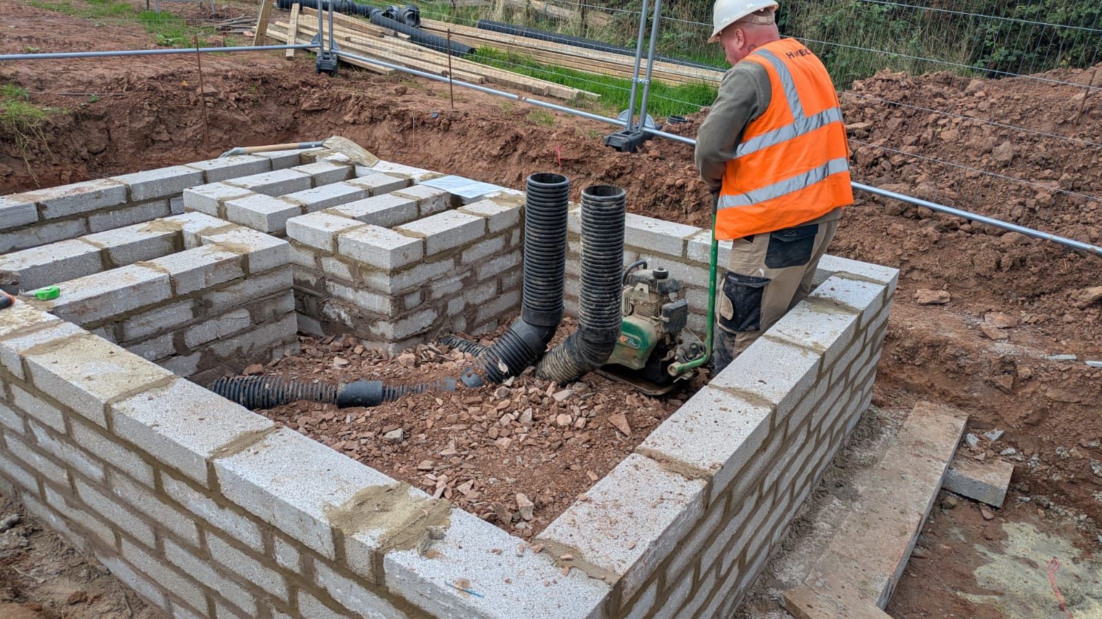 An HWBC operative building a blockwork base for a DNO RMU (ring main unit), with cable ducts brought up through the stone fill.