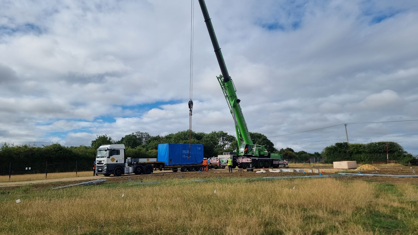 A mobile crane lifting a wrapped switchgear and transformer unit from a low-loader in Cambridgeshire.