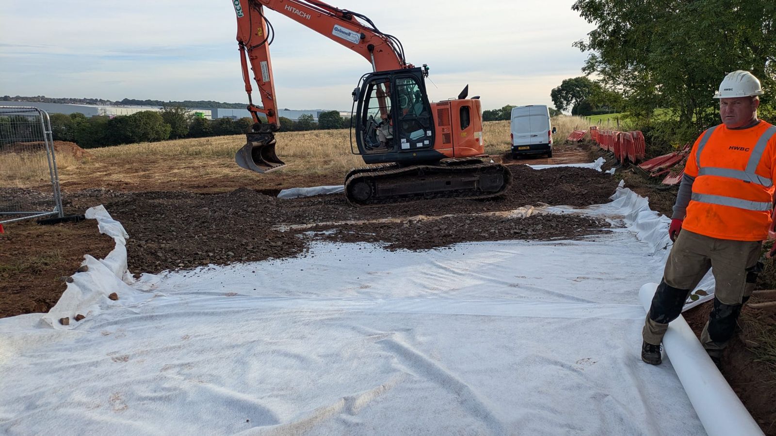 An HWBC operative rolling out geotextile membrane as an excavator spreads stone over it.