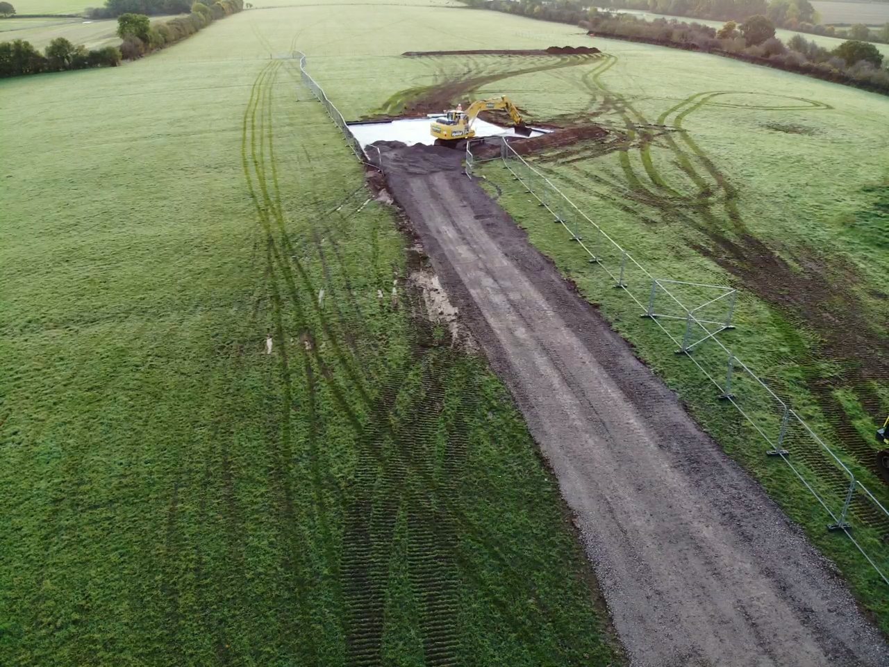 Aerial view of a completed stone haul road running across grass fields with a tipper lorry on it.