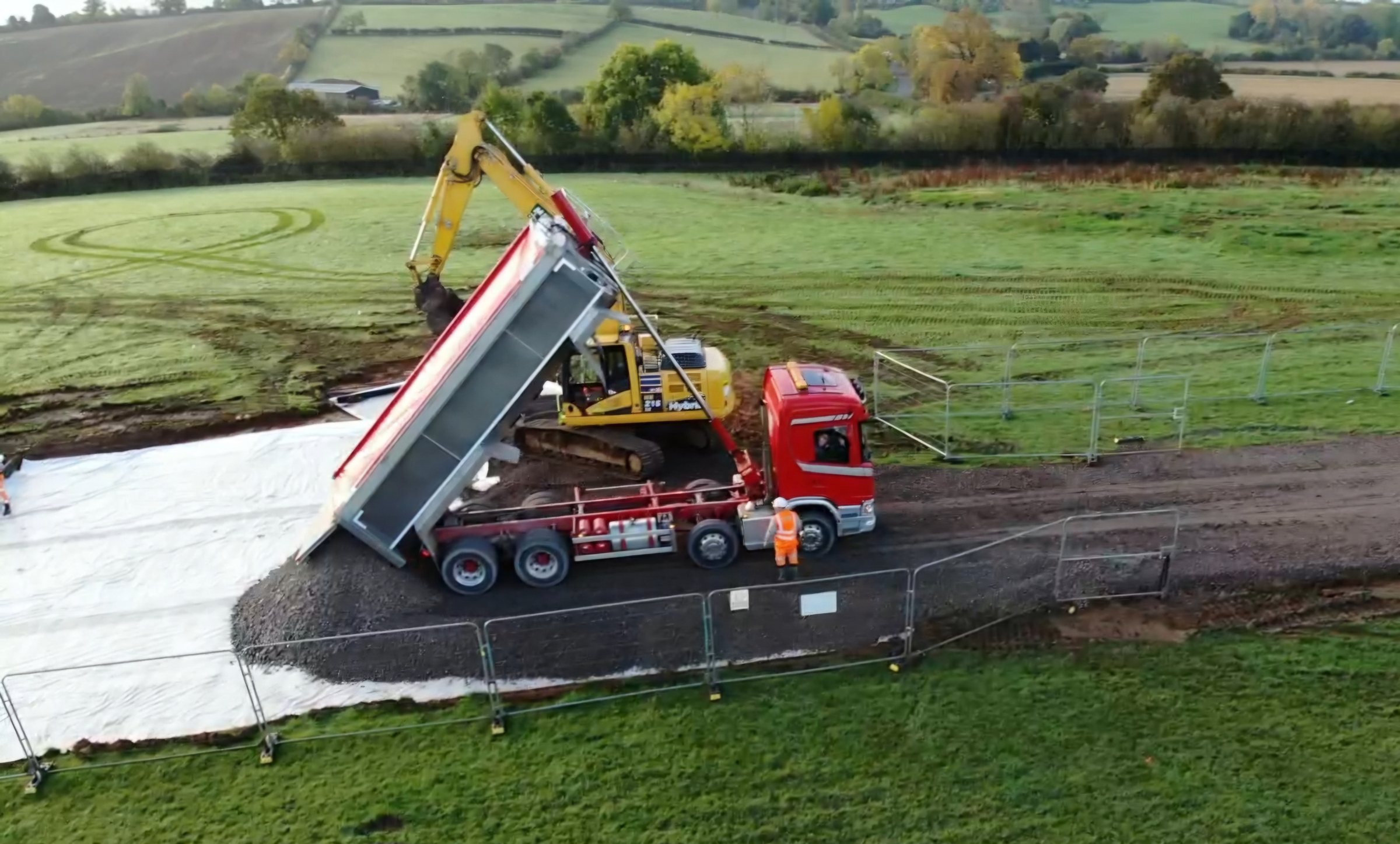 Stone being tipped onto geotextile membrane during construction of a haul road across a field at a renewable energy site.